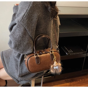 Detail einer braunen Boston-Tasche aus Leder mit Plüschanhänger und goldenen Reißverschlüssen