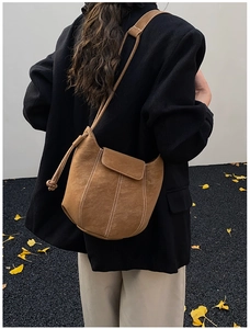 Brown frosted leather bucket bag with white stitching detail worn by a model outdoors
