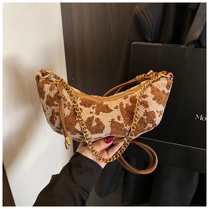 Detail of crescent shoulder bag featuring brown cow print fabric and chunky gold chain