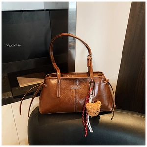 Detail of a brown leather tote bag with metal nameplate and cute bear plush charm
