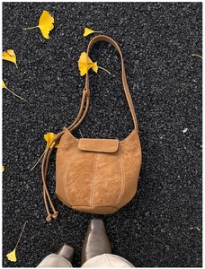 Close-up of a brown suede bucket bag with contrast stitching and tassels on fallen leaves