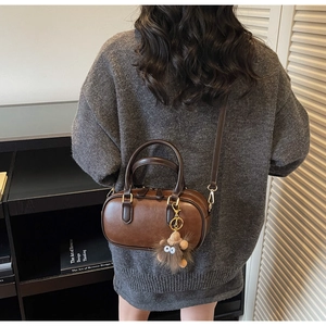 Detail einer dunkelbraunen Bowlingtasche mit Monsteranhänger auf einem grauen Pullover