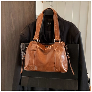 Detail of glossy brown leather tote bag showing wide handles and silver metal hardware