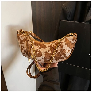 Detail of cow print crescent bag featuring gold chain strap and brown leather handle