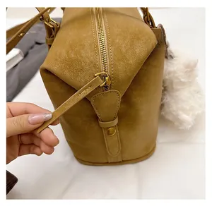 Close-up of smooth gold zipper and soft white pompom charm on a brown leather bag