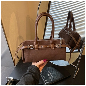 Close-up of brown suede pillow bag with leather handles and decorative metal buckles
