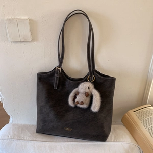 Detail of dark brown tote bag with gold brand logo and cute rabbit charm on white surface