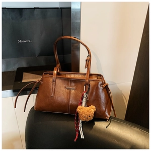 Close-up of brown faux leather tote with metal logo and cute plush bear keychain
