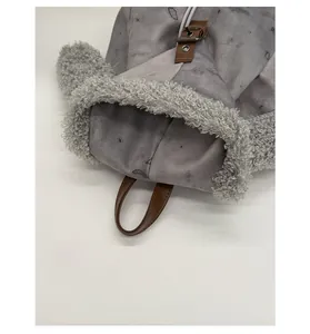Detalle de mochila de ante gris con ribete de forro polar y asa de cuero marrón