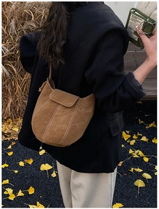 Detail of a brown suede bucket bag with contrast stitching in an autumn park setting