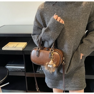 Brown leather Boston bag detail with plush monster charm and adjustable shoulder strap