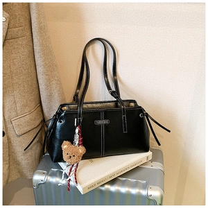 Detail of black leather tote bag with white stitching and cute brown plush bear charm
