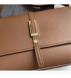 Detailed macro view of the brown lychee grain leather bag with elegant golden metal buckle