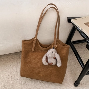 Detailed close-up of brown suede tote bag with brand logo and plush rabbit charm
