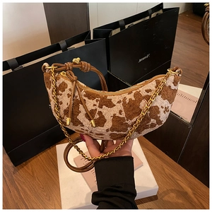 Detail of cow-print crescent bag with golden chain and leather strap on a table