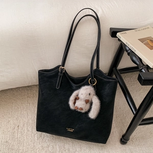 Detail of black tote bag with white contrast stitching and grey plush rabbit charm