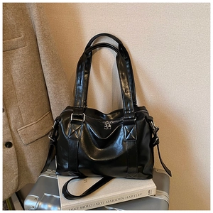 Detail of black glossy tote bag with silver hardware placed on a silver suitcase