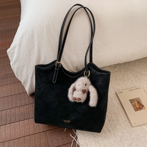 Close-up of black matte leather tote bag with white stitching and plush rabbit pendant