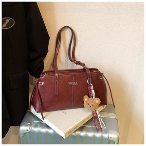 Detail of burgundy leather tote bag with contrast stitching and teddy bear charm