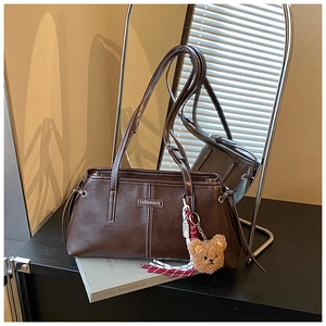 Detail of dark brown faux leather tote bag with white contrast stitching and bear charm