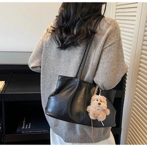 Détail d'un sac cabas plissé noir avec breloque ours, porté par un mannequin en pull gris
