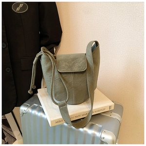 Sage green bucket bag with drawstring detail and flap closure for casual commuting