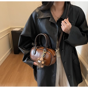 Detail of retro brown leather cylinder bag with cute plush monster charm and gold hardware