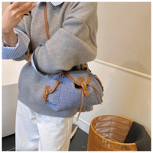 Detail of blue denim bucket bag with drawstring closure and brown leather trim on a model
