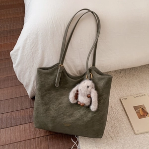 Detail of dark olive green tote bag with gold brand logo and cute plush rabbit charm