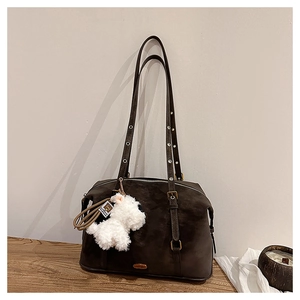 Detail of dark brown suede shoulder bag featuring metal eyelets and a white plush puppy charm