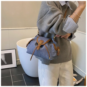 Detail view of denim texture shoulder bag with brown leather trim and gold buckle