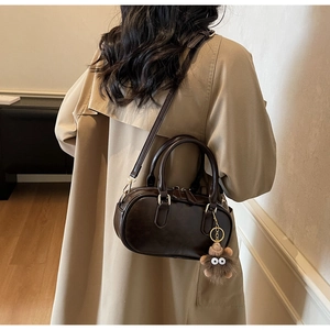 Detail of dark brown Boston bag featuring golden hardware and a plush monster charm