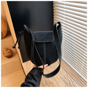 Detail of black suede bucket bag featuring white contrast stitching and thick shoulder strap