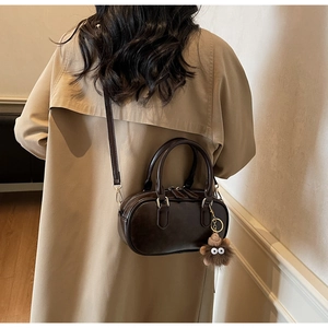 Detail of dark brown Boston bag with plush monster charm and adjustable shoulder strap