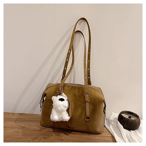 Detailed shot of brown suede shoulder bag with plush dog charm on wooden surface
