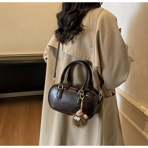 Detail of a dark brown vintage barrel bag featuring a playful furry charm on shoulder strap
