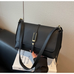 Detail of black litchi texture leather handbag with golden U-shaped metal buckle accent