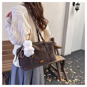 Detail view of coffee suede tote bag with plush charm on a model in autumn garden