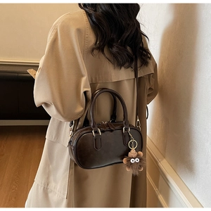 Detail of chocolate brown Boston bag with plush monster charm on khaki trench coat