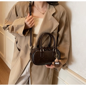 Brown vintage bowling bag with plush charm styled on a beige trench coat