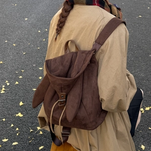 Detail of dark brown faux suede backpack with cute bunny ears on autumn leaf background