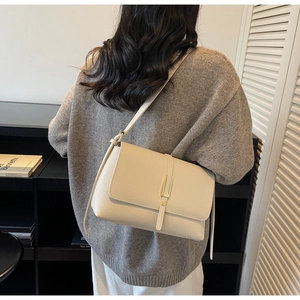 Detail view of a cream beige pebbled leather shoulder bag shown on model in home setting