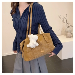 Close-up of vintage brown tote bag with metal logo and cute white plush dog charm