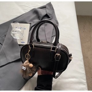 Detail of dark brown Boston bag with golden hardware and fuzzy monster pendant