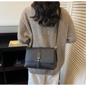 Close-up of black lychee-grain leather texture and golden metal buckle on shoulder bag