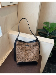 Detailed view of leopard print bucket bag with black leather trim and logo on wooden steps