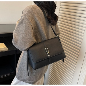 Detail of black pebbled leather texture and gold metal bar buckle on flap shoulder bag