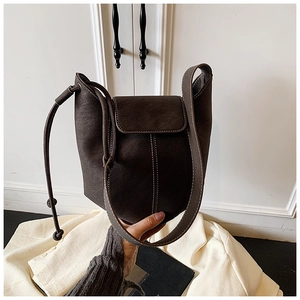 Detail of dark brown bucket bag with contrast stitching and drawstring on beige blazer