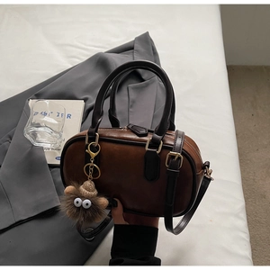 Detail view of brown vintage Boston bag with golden buckle plush monster charm on grey suit