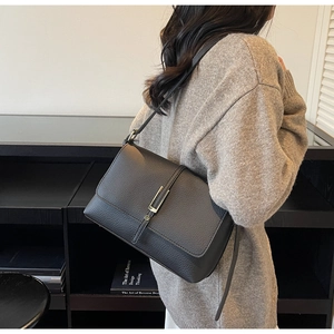 Detail of black litchi grain shoulder bag featuring a sleek silver metal bar fastener